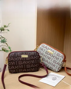 Macro view of patterned double-zip crossbody bags with SAKM monogram on wooden shelves