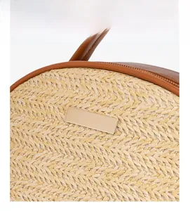 Detail der handgewebten Strohtasche mit braunem Lederbesatz und goldener Metallmarke
