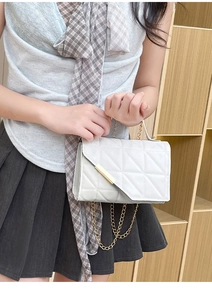 Detail of white quilted handbag with golden metal bar and chain strap for women