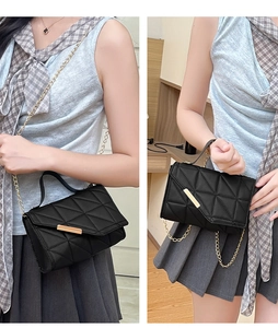 Detail of black quilted leather handbag with gold chain strap and metal bar clasp