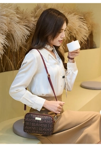 Detail of a brown printed crossbody bag with gold zippers and maroon leather strap