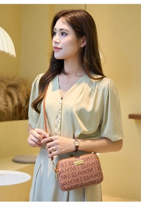 Detail of tan crossbody bag with SAKM monogram pattern and gold brand logo plate