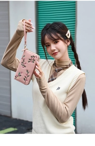 Pink long wallet with floral embroidery and wrist strap shown in an outdoor lifestyle setting