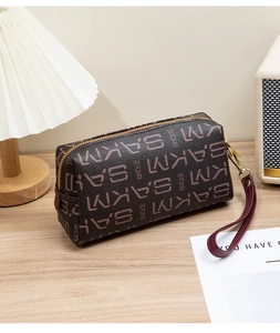 Detail of vintage coffee clutch bag with monogram pattern and gold zipper on wooden desk