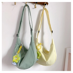 Détail de sacs bandoulière demi-lune en toile avec breloques fleurs et bandoulière