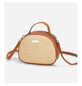 Details der gewebten Strohtextur und braunem Lederbesatz an der halbrunden Handtasche