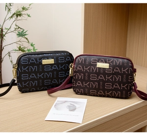 Detail view of dual-layer crossbody bags with SAKM monogram in navy and burgundy colors