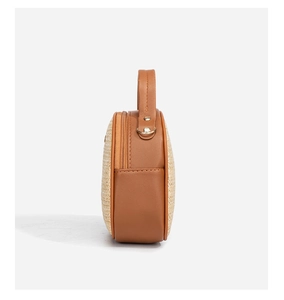 Detailansicht der runden Strohhandtasche mit braunem Lederbesatz und Metallreißverschluss