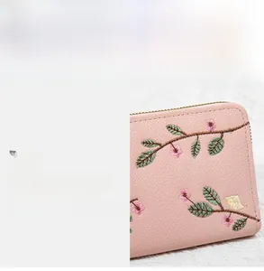 Detail of pink floral embroidery and grainy faux leather texture on long clutch wallet