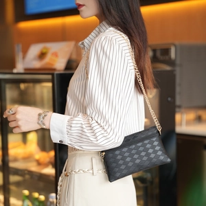 Borsa a tracolla trapuntata nera con catena dorata indossata da modella in un caffè