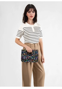 Lifestyle shot of a sequined square handbag styled with a casual polo and trousers
