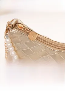 Detailansicht der goldenen Stepptasche mit glattem Reißverschluss und eleganter Perlenkette