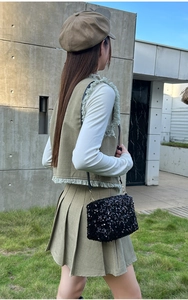 Detail of a black sequin shoulder bag paired with an olive green fringe vest and skirt