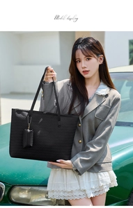 Detail of black woven large tote bag with a matching small charm held by a model
