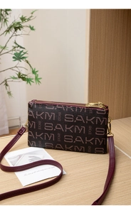 Detail of burgundy crossbody bag with SAKM logo pattern and gold zipper hardware