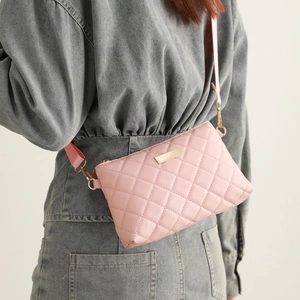 Detailed view of pink quilted crossbody bag with gold metal plate and textured fabric strap