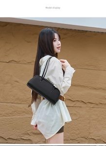 Sac baguette moderne en cuir noir présenté sur un fond de mur en pierre texturée