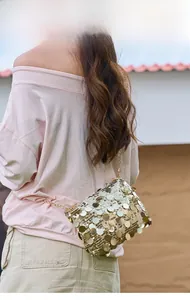 Outdoor model shot showing the back view of a shimmering gold sequin chain shoulder bag