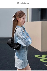 Close-up of black pleated underarm bag in matte leather worn by a model in the city