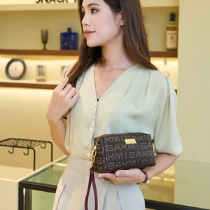 Brown SAKM monogram clutch bag with gold zipper and wrist strap held by model