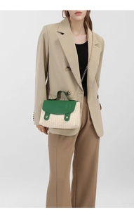 Detail of woven straw and dark green leather satchel with elegant gold chain strap