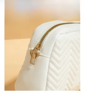Detail of white quilted crossbody bag showing chevron stitching and gold metal zipper