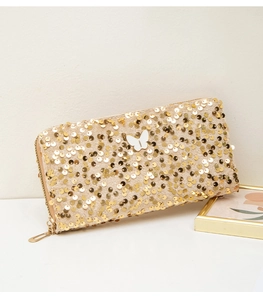 Detail of long gold sequin wallet featuring a white butterfly ornament and metal zipper
