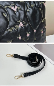 Detail of floral embroidery on black quilted tote with adjustable gold-tone shoulder strap