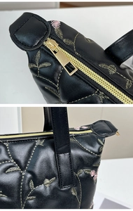 Close-up of golden zipper and floral embroidery on black quilted leather handbag