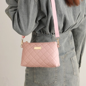 Detail of pink quilted crossbody bag featuring gold hardware and a wide fabric strap