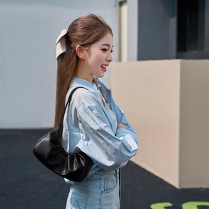 Minimalist black pleated cloud bag shown with casual light blue cardigan and jeans outfit
