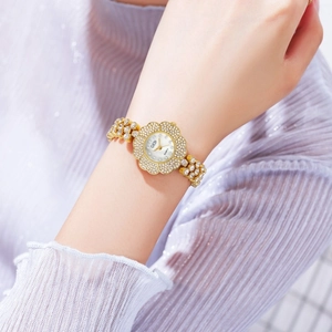 Détail d'une montre à quartz dorée en forme de fleur avec strass sur un poignet féminin