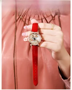 Detail of red lizard-grain leather strap and rose gold rhinestone watch with deer relief