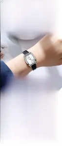 Détail de montre tonneau argentée avec chiffres romains et bracelet en cuir noir