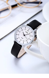 Close-up of GEDI quartz watch with white dial and black leather strap by a ceramic cup
