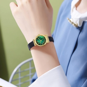 Vintage women's watch with green dial, gold case, and black leather strap worn on wrist
