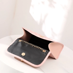 Pink quilted crossbody bag with gold chain strap and magnetic snap closure on marble base
