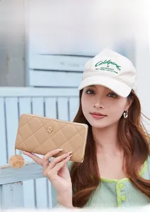 Close-up of quilted khaki wallet featuring a gold flower clasp and plush faux fur pompom