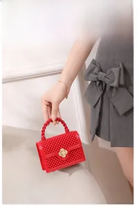Détail du sac en gelée ajouré rouge avec fermoir trèfle doré et texture perlée