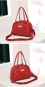 Detail of red quilted Boston bag with gold plaque and adjustable strap on a table