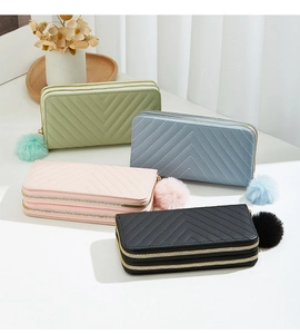 Close-up of four quilted dual-zipper purses with fluffy pompom charms in soft pastel colors