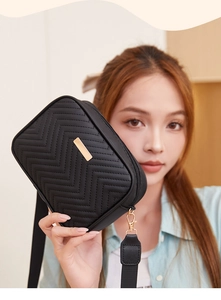 Detail of black V-quilted camera bag featuring gold metal plaque and removable strap