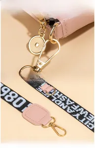 Détail macro du sac en cuir rose avec quincaillerie dorée et bandoulière en toile logotée