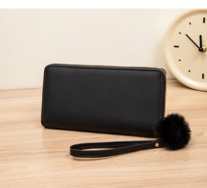 Close-up of black long wallet with smooth texture, wrist strap, and decorative pompom