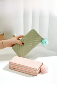 Detail of long quilted PU leather wallets in mint and pink with pompom zipper charms