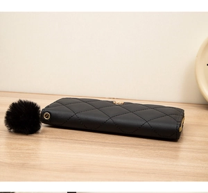 Detail of black quilted long wallet featuring a fluffy pom pom and gold zipper hardware