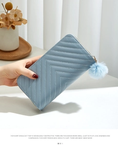 Detail view of light blue quilted wallet with golden zipper and soft pom-pom keychain