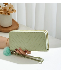 Detail of light green quilted long wallet with double zippers and pom-pom charm