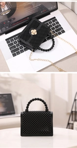 Gros plan d'un mini sac gelée noir à texture perlée avec fermoir fleur dorée sur laptop