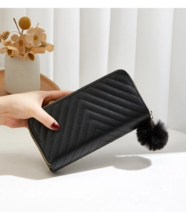 Detail of black quilted leather long clutch with gold zipper and faux fur pompom charm